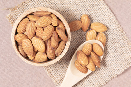 Almond seeds in a cup and spoon are placed on a woven sack and wood table top in a high angle.の写真素材