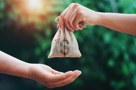 hand giving money bag to another people on green background with sunriseの写真素材