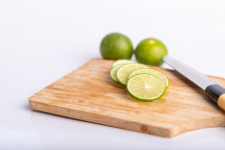 Close up sliced of the green lime and seed with a knife place on wooden board in a kitchen on white...