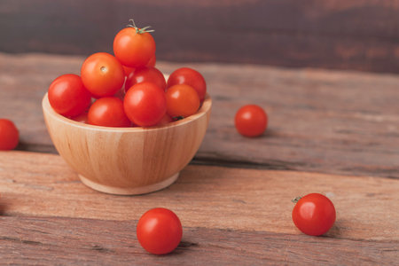 Group tomato in a wood bowl place on the wooden table. Cherry tomatoes is a small that has a sweet, firm texture and has a pleasant aroma. And contains beta-carotene, vitamin C and high vitamin E.の写真素材