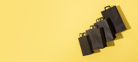 Black shopping bags on black friday sale yellow background with copy space. Banner formatの写真素材