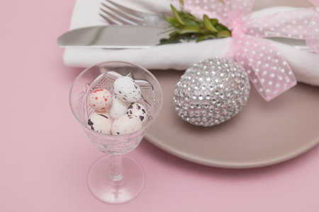 Glass with Easter eggs on the background of plates and cutlery. Variative focus.