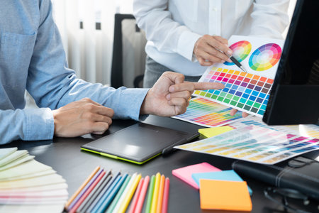 graphic designer team working on web design using color swatches editing artwork using tablet and a stylus at desks In creative office.の写真素材