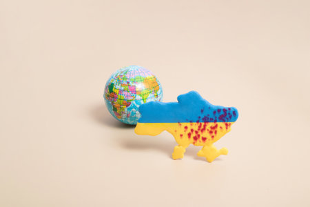 Plasticine yellow and blue map of Ukraine with blood shots and the planet Earth behind. Ukraine...