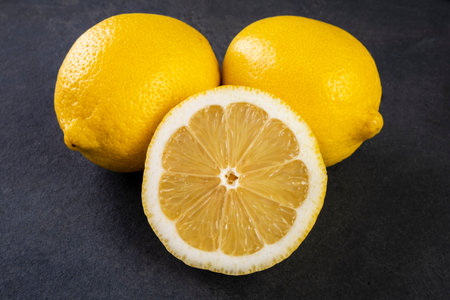 two whole Sicilian lemons and one half on a dark slate stone.の写真素材