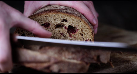 slicing a loaf of unusual bread made using dried cranberries and wheat and rye flour, the bread is rearranged to another placeの写真素材