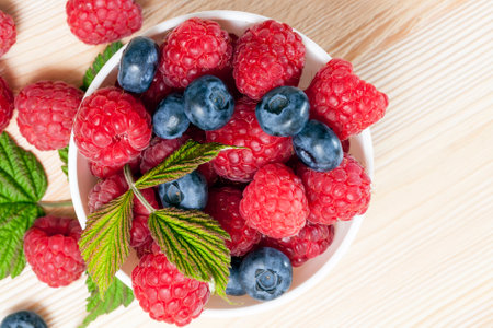 raspberries and blueberries in a white plate standing on a table, top view close-up