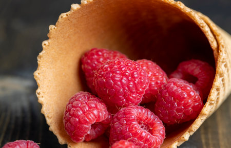 Red ripe raspberries with waffle cups on a black table, delicious raspberries in an ice cream cupの写真素材
