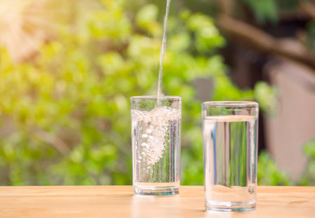 The pure water from jug into glass on wooden table on nature background.の写真素材