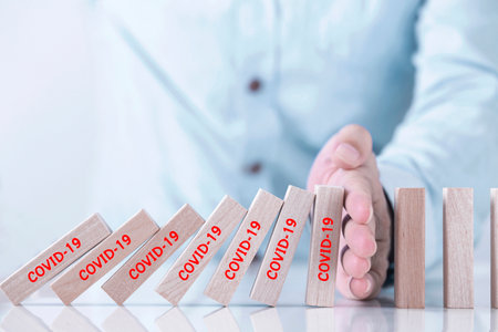 Businessman hand stopping the domino represents pandemic COVID-19 virus effect  , Stop the spread of...