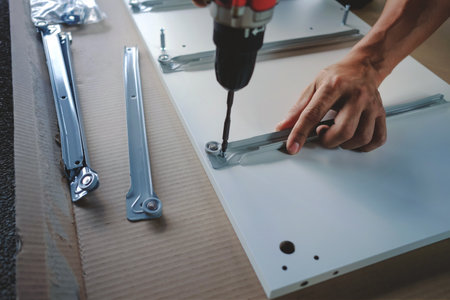 Assembling Furniture at Home. Moving for a New House or DIY Concept. Craftsman using Cordless Screwdriver to Installing the Cabinet.の写真素材