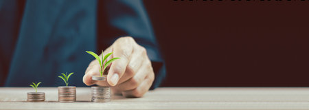 Close up of hand stacking gold coins with green bokeh background ,Business Finance and Money concept,Save money for prepare in the future.Trees growing on coin.vintage process styleの写真素材