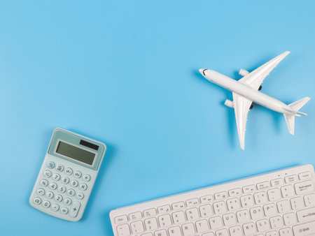 Top view or flat lay of airplane model, computer keyboard, and blue calculator  on blue background, business and traveling budget concept.の写真素材