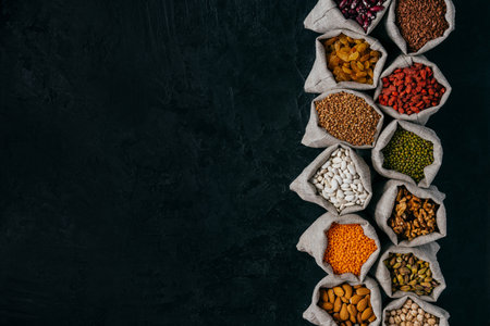 Photo of healthy food ingredients in little sacks, isolated over black background with empty space for your promotion. Bags of cereals and beans, fruit in one rowの写真素材