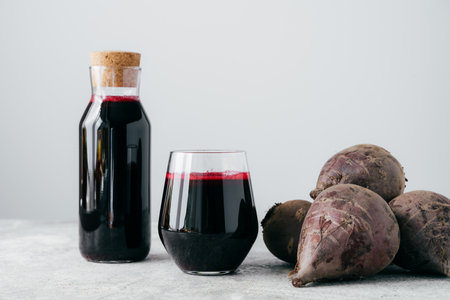 Fresh bright beetroot juice in glass bottle, raw red beet near, isolated over white background....