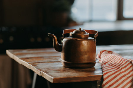 Horizontal shot of aluminium teapot on wooden table against blurred background striped napkin near. Old kettle made of bronzeの写真素材