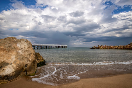 Low angle view of the sea with a pier and big rock on shoreの写真素材