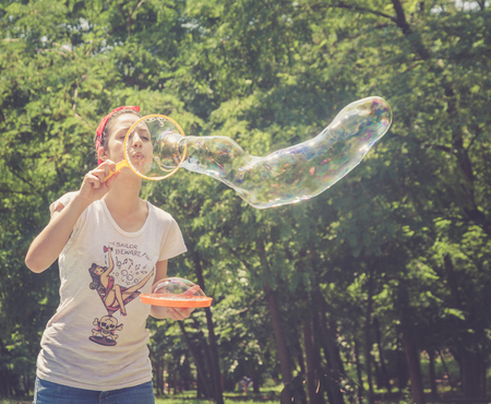 Happy young girl has fun with bubbles on a summer day in a park. She is smiling. She has tattoos and...