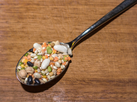 every sort of legumes inside a spoon on a wooden chopping boardの写真素材