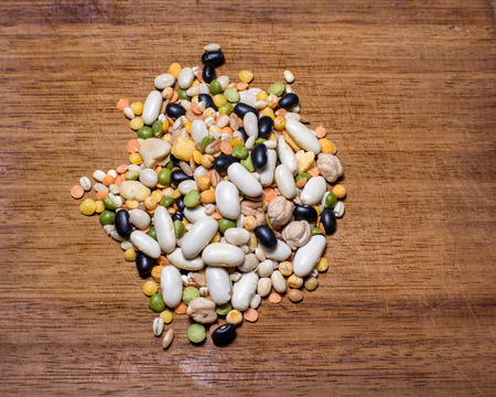 handful of every sort of legumes on a wooden chopping boardの写真素材