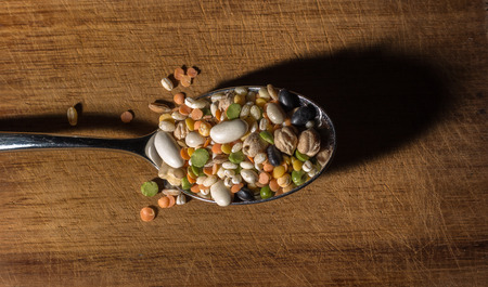 every sort of legumes inside a spoon on a wooden chopping boardの写真素材