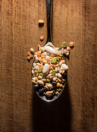 every sort of legumes inside a spoon on a wooden chopping boardの写真素材