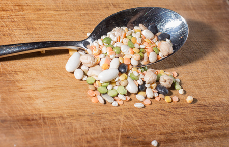 every sort of legumes inside a spoon on a wooden chopping boardの写真素材