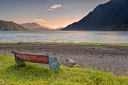 Bench on the beach near the town of Hornopiren with a peaceful view on the Comau fjord at sunset. The Comau fjord, also known as Leptepu, penetrates the mainland of Chile, in Los Lagos Region.の写真素材