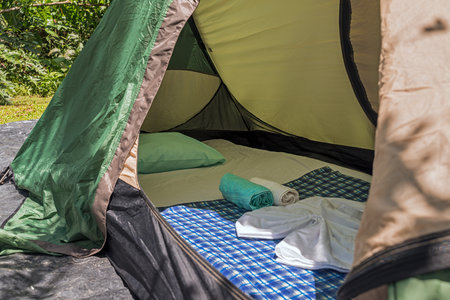 Horizontal close-up view inside of a green tent with mattress, cushion, sheet and towelsの写真素材