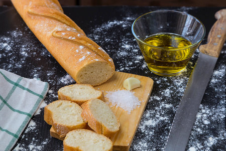 Loaf of bread on a board with cut pieces against a black backgroundの写真素材