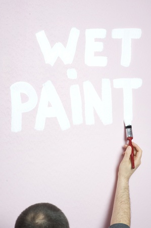 man painting words ' wet paint' on a pink wallの写真素材