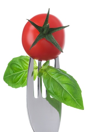 cherry tomato and basil leaves on a fork against a white backgroundの写真素材