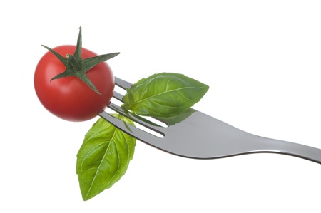 cherry tomato and basil leaves on a fork against a white backgroundの写真素材
