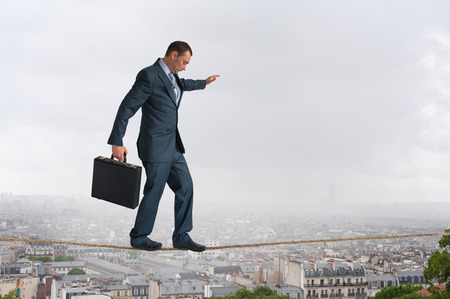 businessman walking across a tightrope above the cityの写真素材