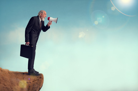 senior businessman yelling through a loudhailer from a cliff edgeの写真素材