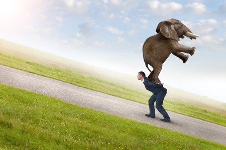 business adversity concept with businessman carrying elephant uphillの写真素材