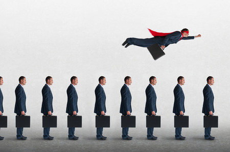 superhero businessman overcoming inertia flying away from a static queue of businessmenの写真素材