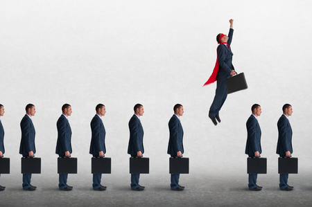 superhero businessman overcoming inertia flying away from a static queue of businessmenの写真素材