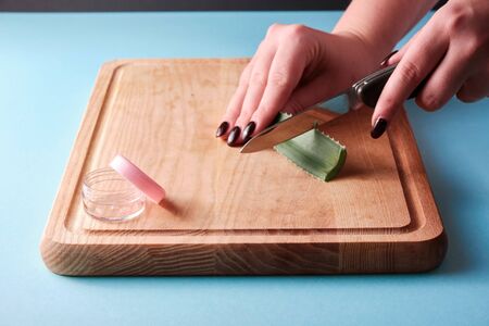 Cutting aloe vera slices with a knife next to a open empty box with pink cap, blue backgroundの写真素材