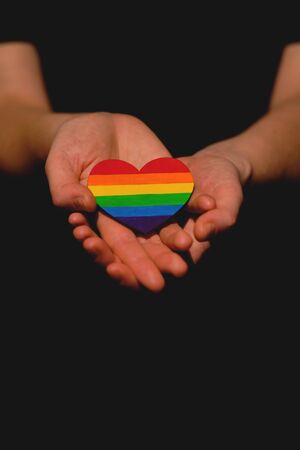 Female arm holding the heart coloured in LGBT pride colours on the dark background. Concept of the International Day Against Homophobia concept, sexual equality, feminism, social safety.の写真素材