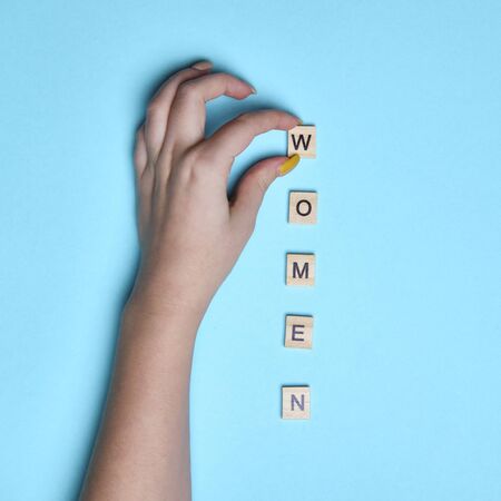 Top view women spelled in wooden blocks on blue background. Woman hand. Love, 8 march background....
