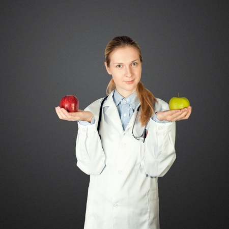 female doctor with green and red apples in her hands, and stethoscope on her neck の写真素材
