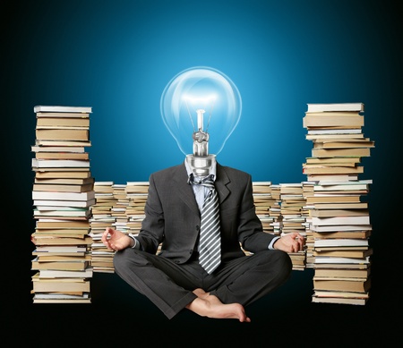 businessman in yoga pose and lamp-head with many books nearの写真素材