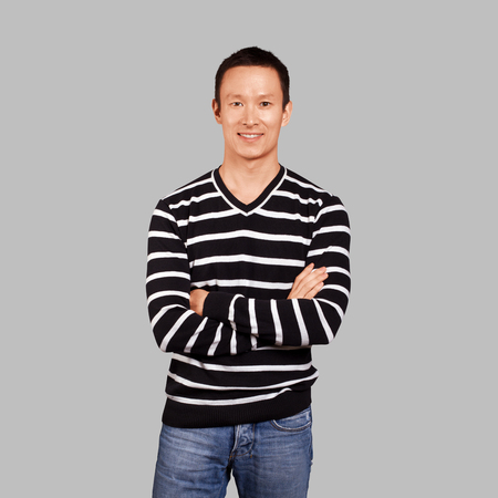 Asian man in striped pullovert, looking on camera, with folded hands, isolated on trendy gradient backgroundの写真素材