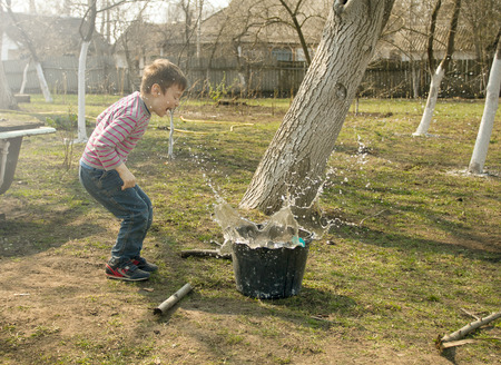 Boy throwing the stone in the bucket with water. Boy playing in the gardenの写真素材