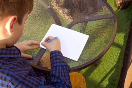 Boy wrtitting something. Boy doing homework outdoors. Boy drawing on paper or wrtitting a letter