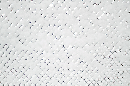 Snow-covered Rabitz grid. Lattice fence covered with fresh snow. Winter background texture. White...