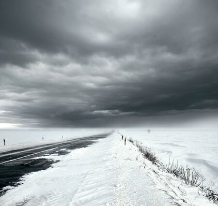 Beautiful stormy sky with clouds and snow road. Snow road in the middle of snow fieldsの写真素材