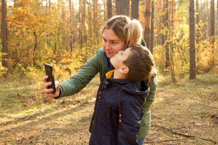 Son and Mother are making selfie in the Park. Boy and Mother have fun in the autumn parkの写真素材