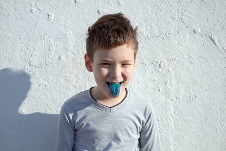 Cute smiling boy against white wall. Boy with blue lollipop. Boy with blue tongueの写真素材